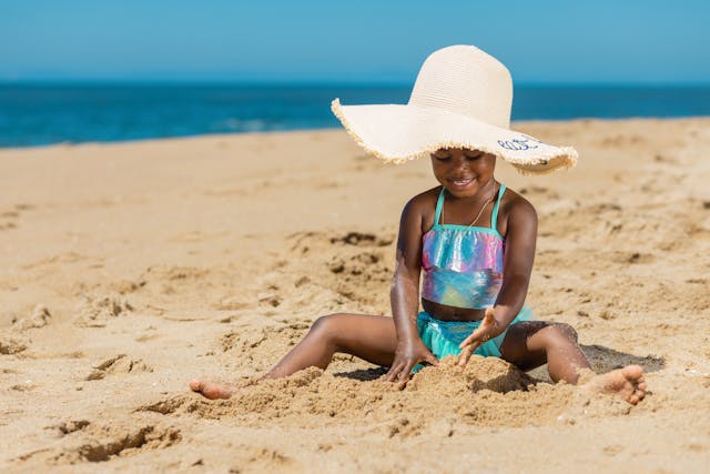 toddler with beach hat playing sand
